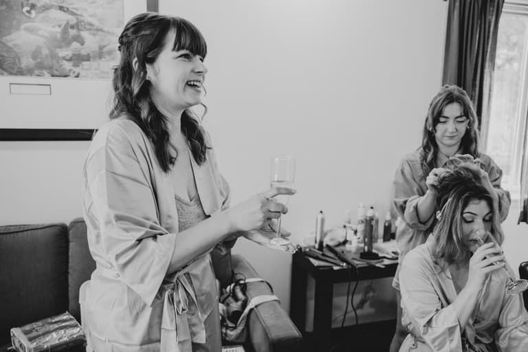 Bridesmaids sharing champagne and laughter while getting ready