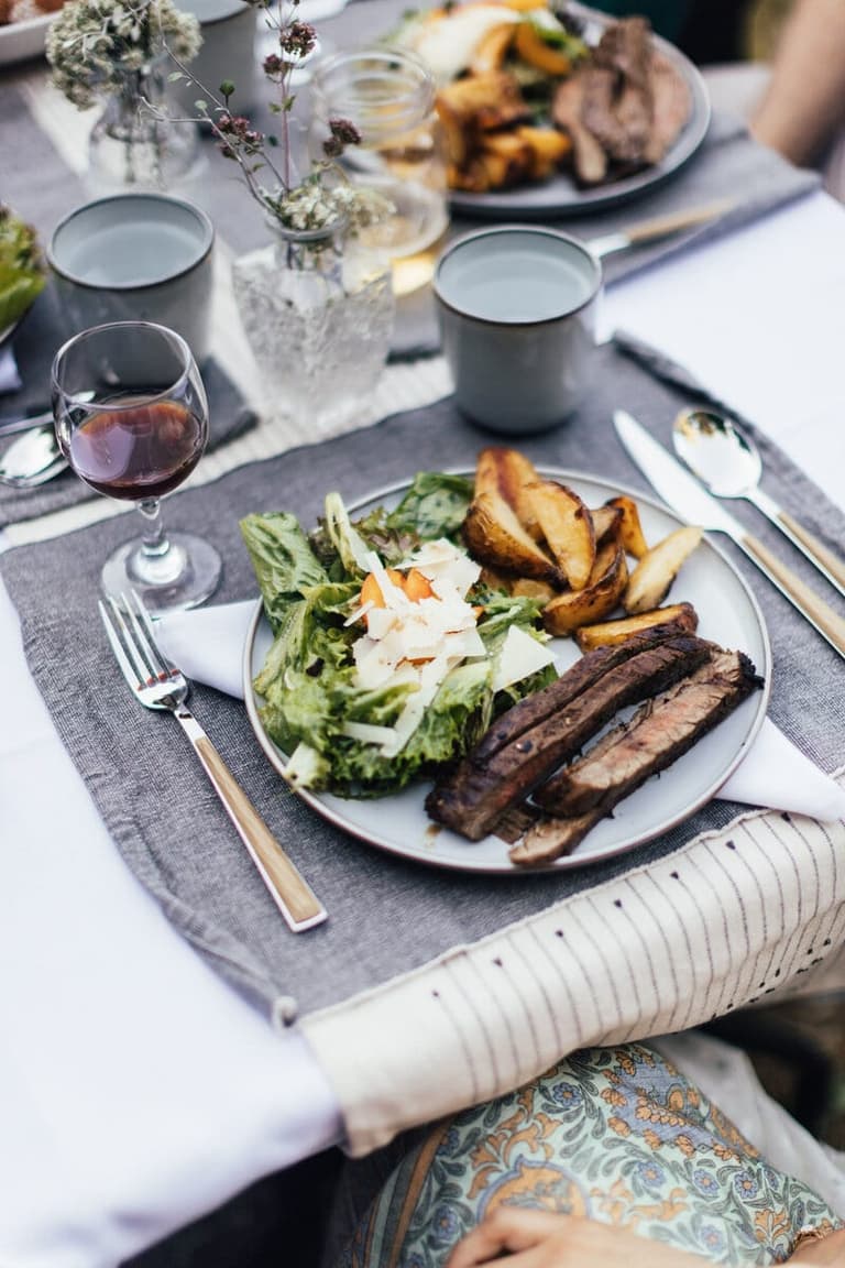 Plated grilled meat, roasted potatoes and greens at a linen-set table