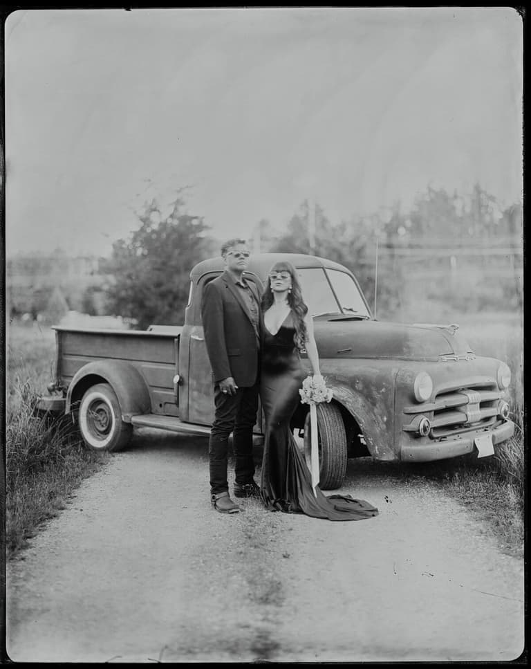 Pair posed beside a vintage pickup truck on a gravel lane