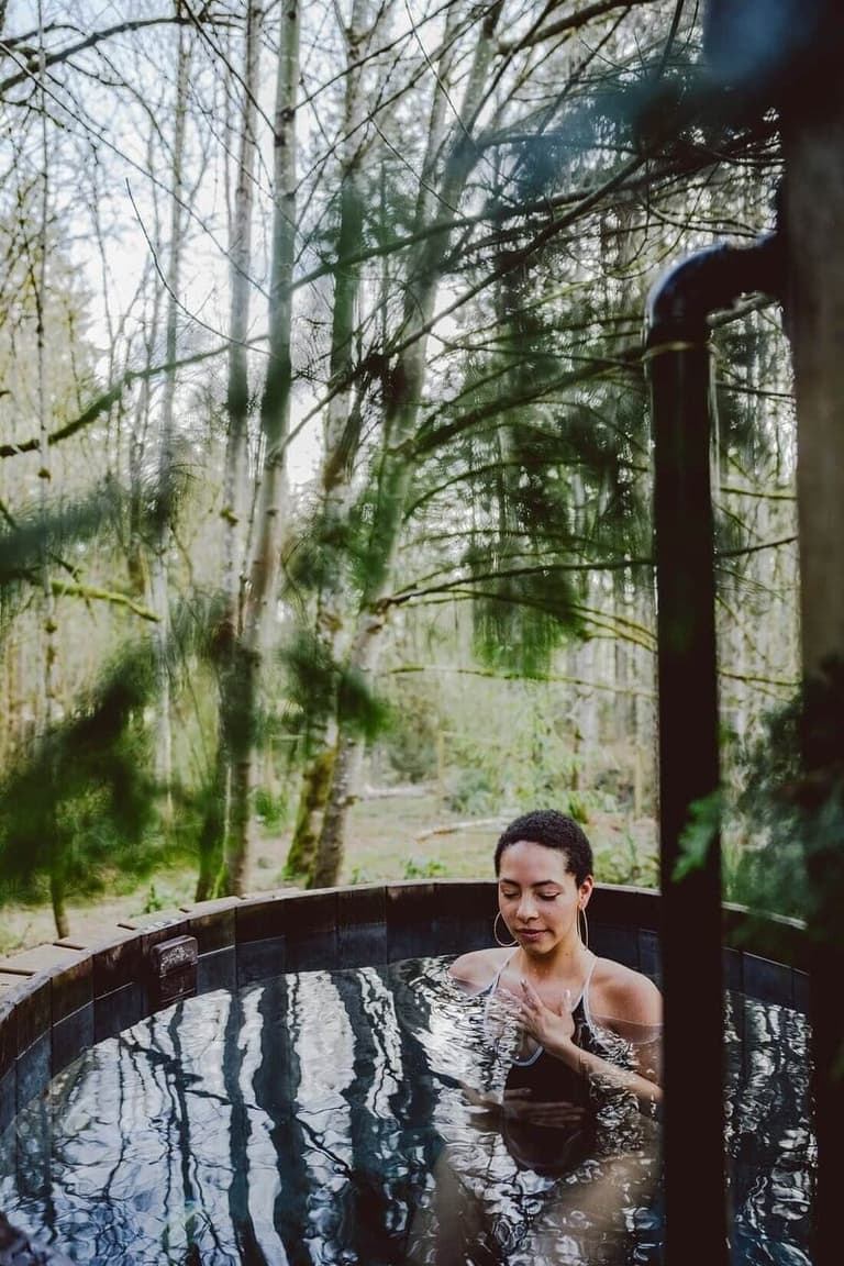 Woman soaking in a forest-side cedar hot tub at Solace Organic Spa