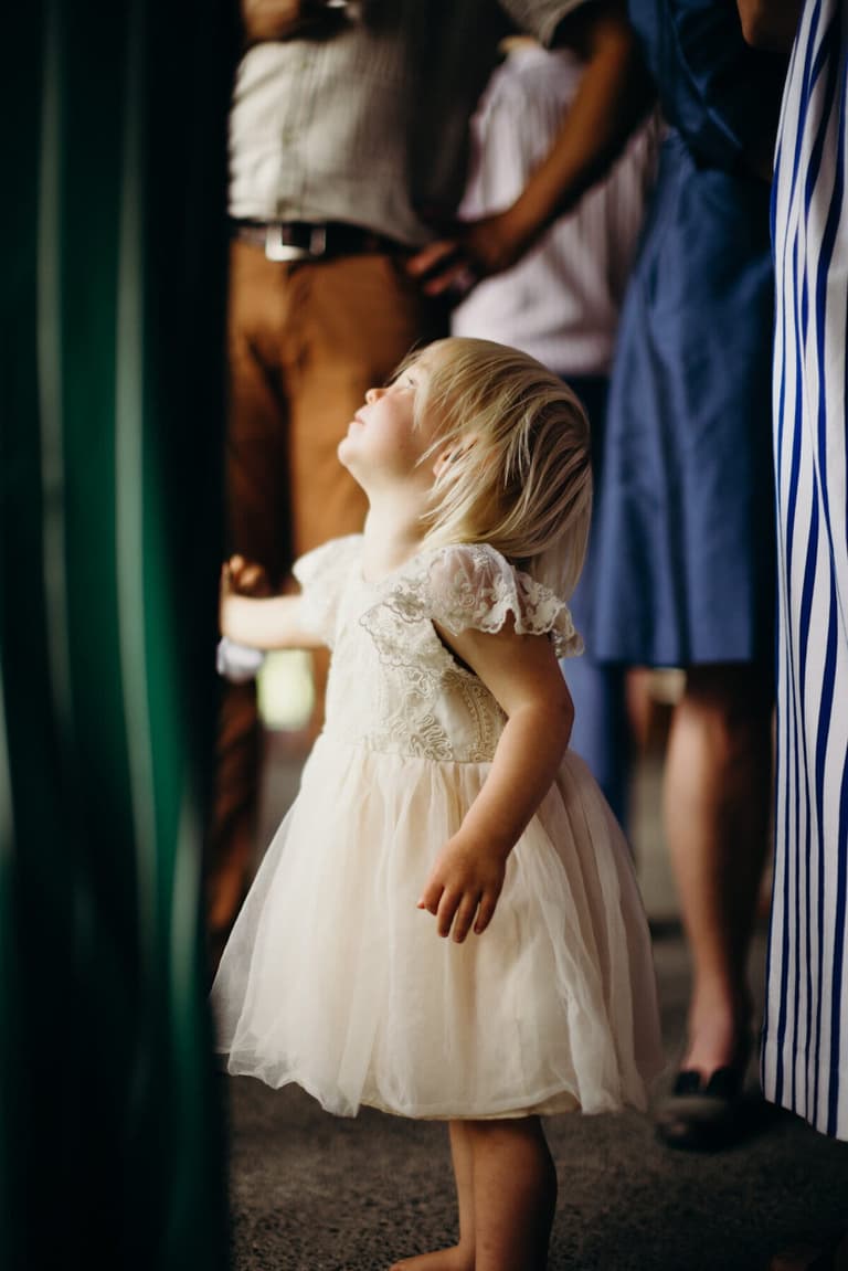 Flower girl in tulle gazing up at wedding guests