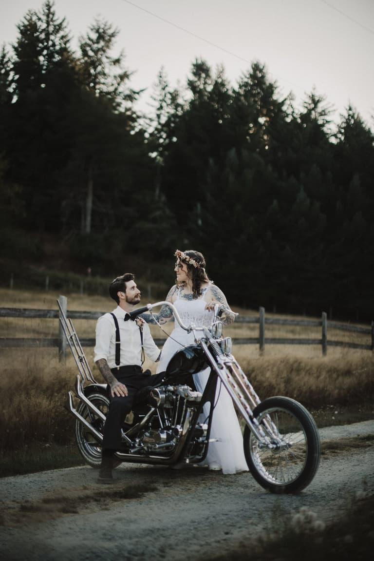 Groom in suspenders on a chopper motorcycle beside his bride