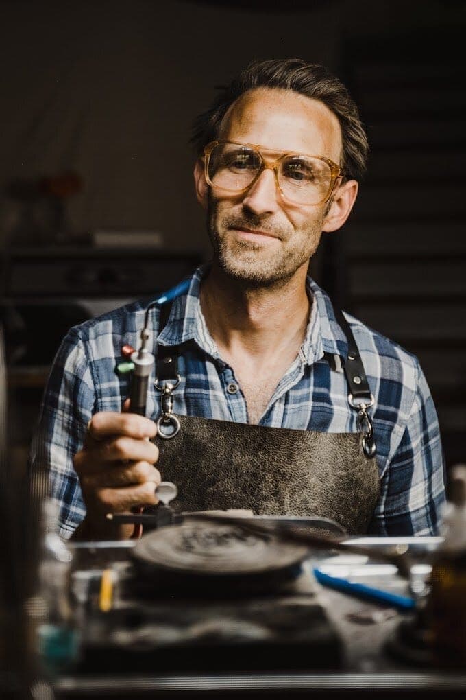 Goldsmith in a leather apron holding a torch at his workbench