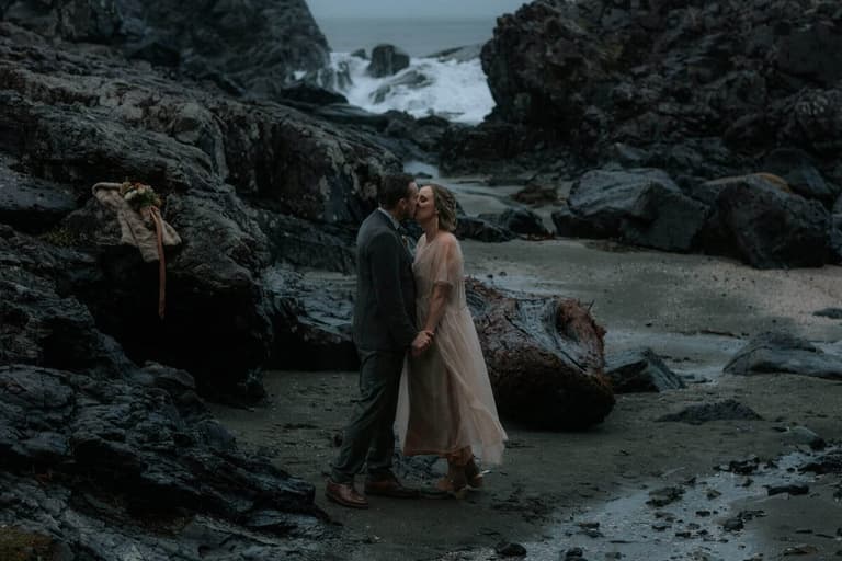 Windswept couple in blush and grey kissing on a stormy beach