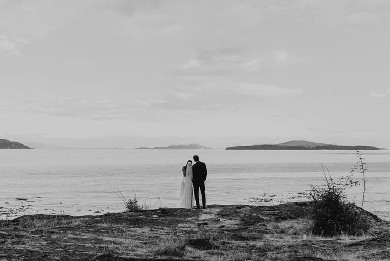 Couple gazing across calm water toward distant islands, black and white