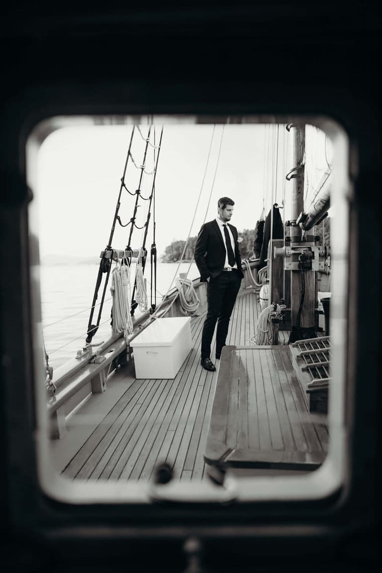 Groom crossing a tall ship deck framed through a cabin window